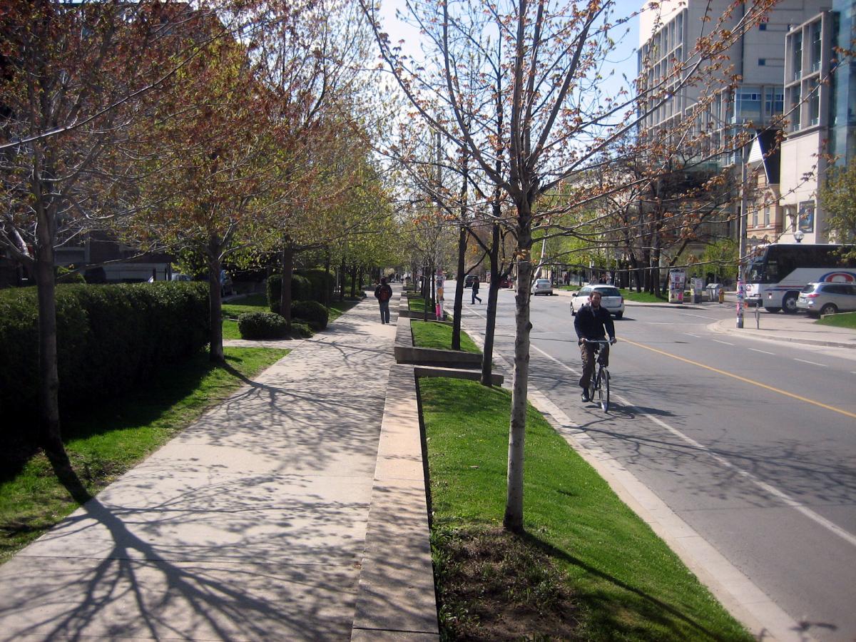 Image of large planters on an urban sidewalk with a cyclist next to it. 